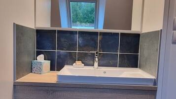 Une salle de bain avec un lavabo intégré, une fenêtre au-dessus du miroir et un porte-serviettes en dessous.