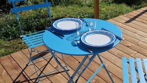 Un juego de mesa azul al aire libre con platos, cubiertos y vasos sobre una terraza de madera.