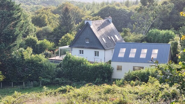 Una casa con techo inclinado, rodeada de abundante vegetación y árboles.