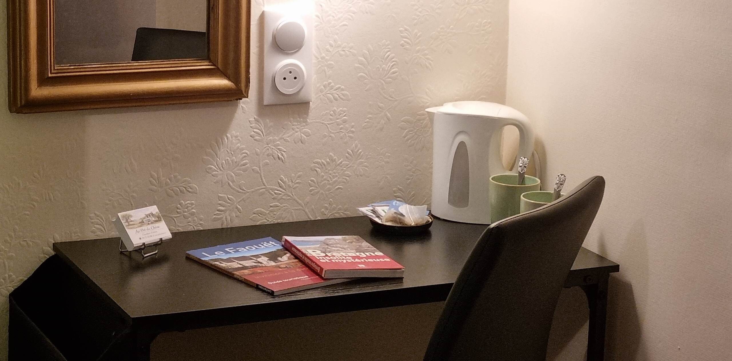 Una camera d'albergo con una scrivania, un bollitore, una tazza e due libri.