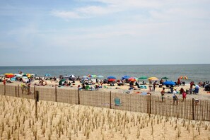 A beach with a wooden fence, umbrellas, and people.