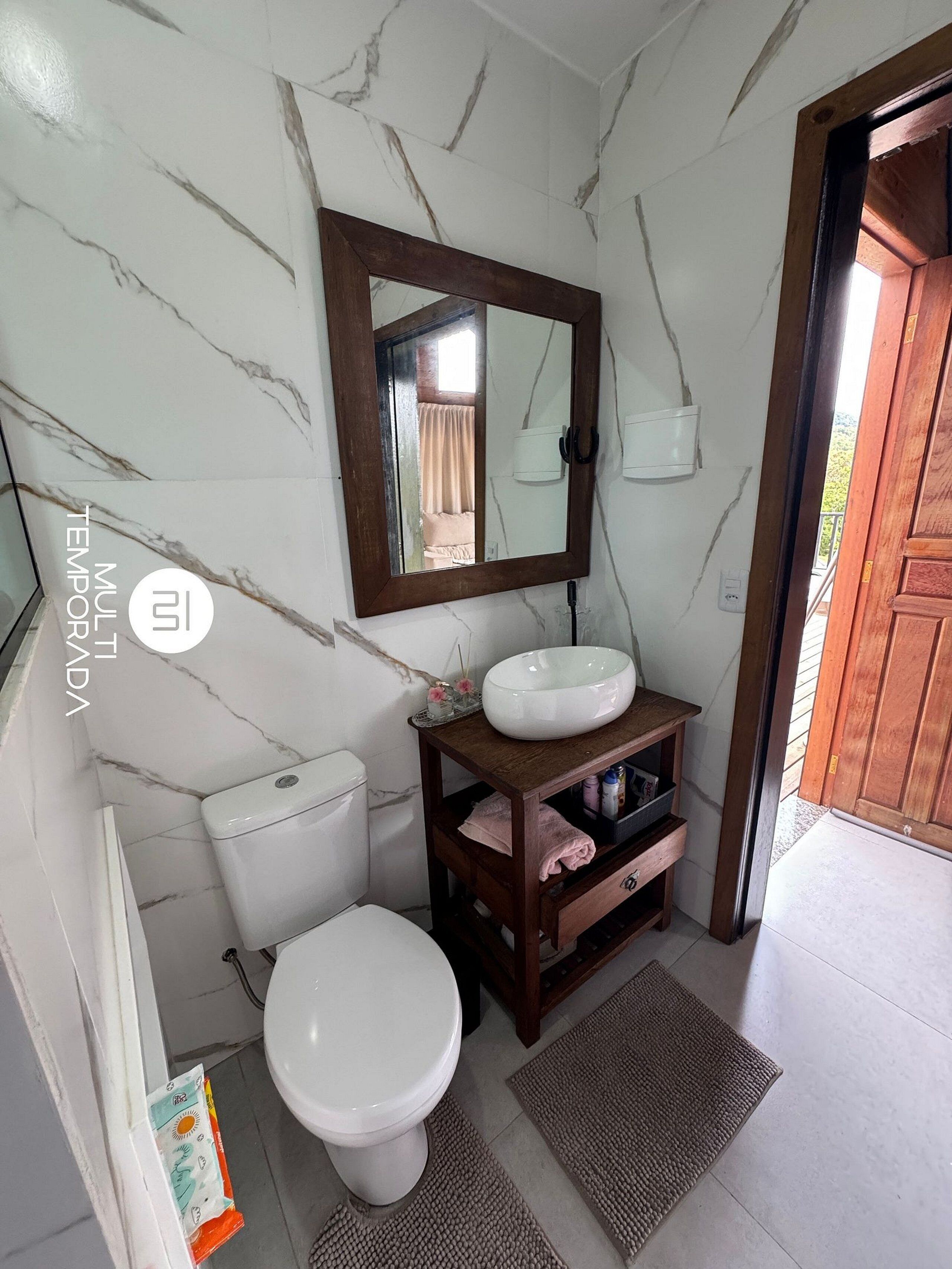 A bathroom with a toilet, a sink, a mirror, and a wooden cabinet.