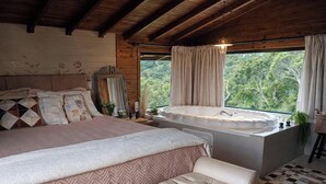 Un dormitori amb un llit gran, una finestra amb cortines, vista a vegetació i una banyera.