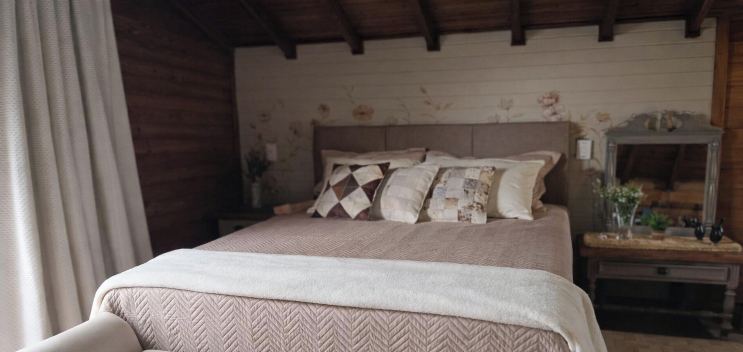 A bedroom with a bed, a nightstand, a mirror, and a wall with floral wallpaper.