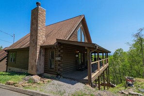 A log cabin with a stone chimney, large windows, and a porch. - Eagles Roost: Stunning Smoky Mountain Views - 2BR/2BA Cabin Retreat, Community Pool (Sevierville)