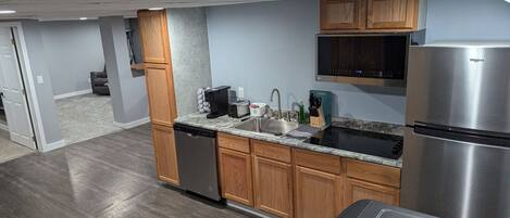 A compact kitchen with wooden cabinets, a stainless steel refrigerator, and a dishwasher.