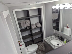 A bathroom with a toilet, a sink, a mirror, and shelves with towels.