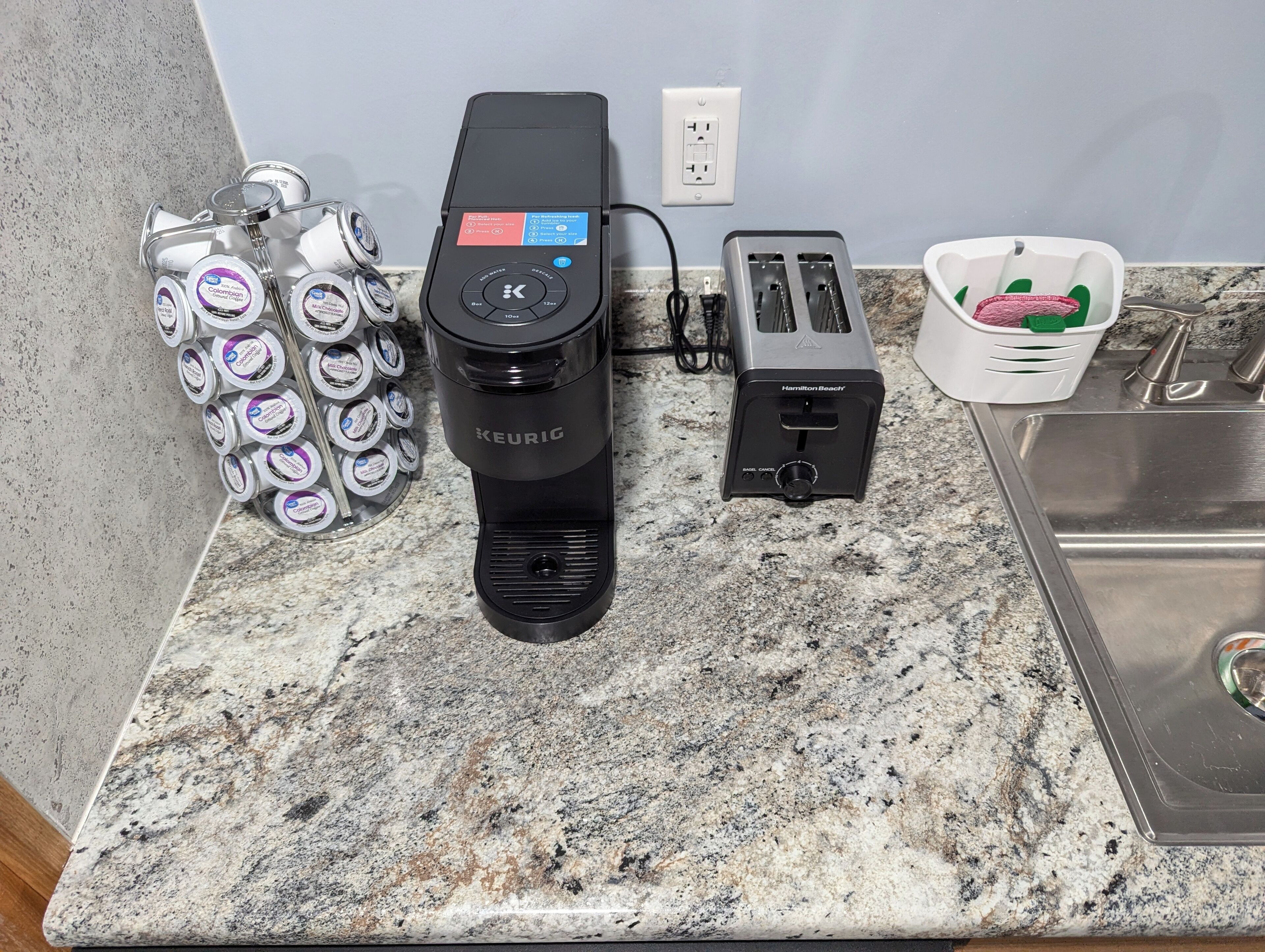 A kitchen counter with a Keurig coffee maker, a toaster, and a basket of coffee pods.
