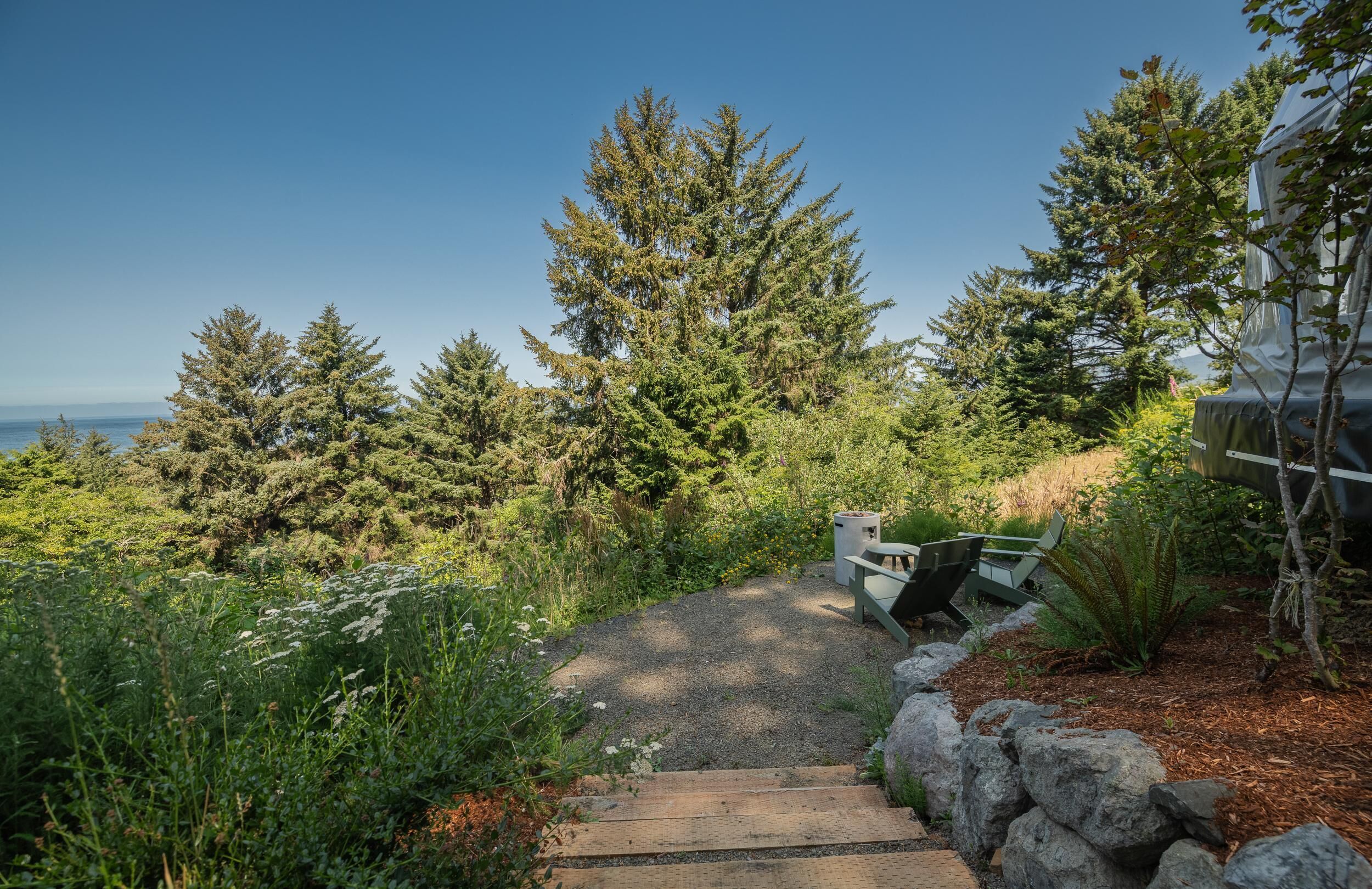 A pathway leading to a seating area with a view of the ocean and dense forest.
