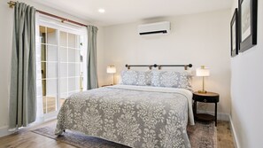 Un dormitorio con cama, dos lámparas de noche, un equipo de aire acondicionado y un ventanal corredero.