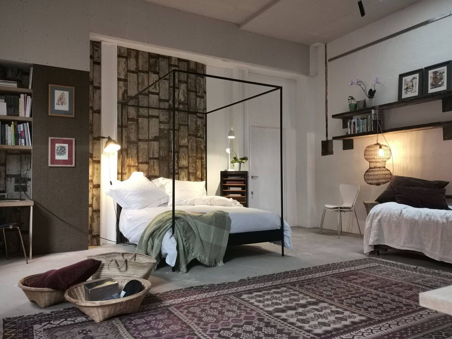 Een slaapkamer met een hemelbed, nachtkastje, stoel, boekenplank en een kamerbreed tapijt met dessin.