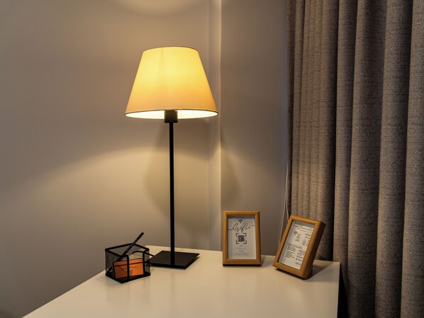 A modern lamp on a bedside table with a framed certificate and a small cube-shaped object.