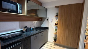 A modern kitchen with a built-in microwave, stove, and dishwasher. There is a wooden cabinet and a mirror above the sink. - Aurea 603 (João Pessoa)
