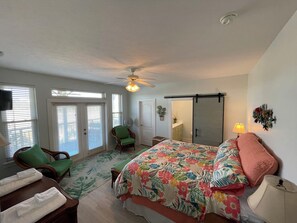 A bedroom with a bed, a chair, a fan, a ceiling fan, and a sliding door.
