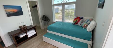 Un dormitorio con una cama grande, una mesita con una cesta, una planta en maceta y vistas al exterior a través de una ventana.