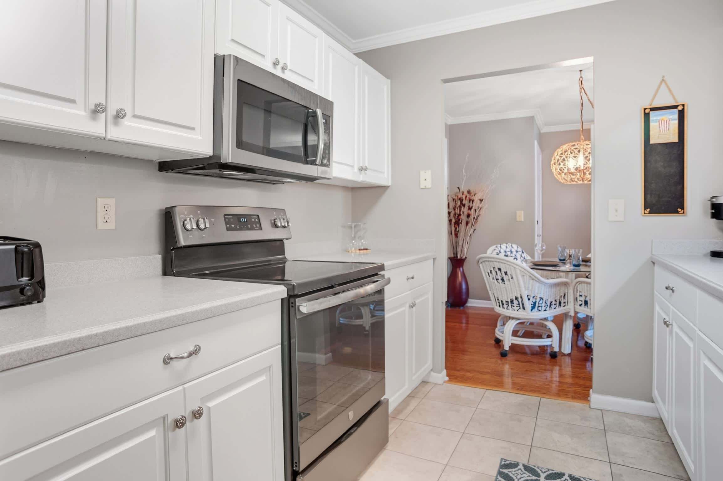 A modern kitchen with white cabinets, stainless steel appliances, and a dining area with a white table and chairs.