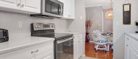 A modern kitchen with white cabinets, stainless steel appliances, and a dining area with a white table and chairs.