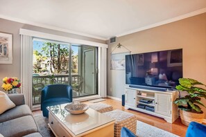 A living room with a TV, a sofa, a coffee table, and a balcony with a chair. - 909 Cutter Court – Modern Coastal Retreat Near Harbor Town Marina (Hilton Head Island)