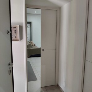 Una stanza con una porta chiusa, un letto e un piccolo oblò con persiane.
