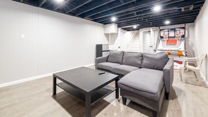A modern living room with a gray sectional sofa, a dark coffee table, and a basketball hoop in the background. - 5BR Home Near Airport, Expo, Downtown Sleeps 12 (Louisville)