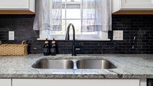 A kitchen with a black tiled backsplash, a stainless steel sink, and a window with sheer curtains. - 5BR Home Near Airport, Expo, Downtown Sleeps 12 (Louisville)