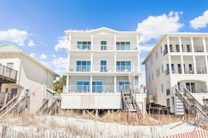 A multi-story beachfront hotel with balconies, a flag, and a sandy foreground. - Gulf Front Home with Private Pool, In-Home Elevator and Movie Theatre (Miramar Beach)