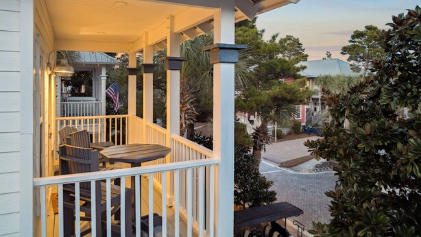A covered porch with outdoor seating, a flag, and a view of the surrounding neighborhood. - Pool Access | LSV | Dogs Welcome (Santa Rosa Beach)