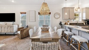 A spacious dining area with a long table, wicker chairs, and a hanging light fixture. - Pool Access | LSV | Dogs Welcome (Santa Rosa Beach)