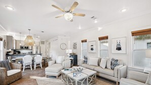 A spacious living area with a kitchen, white furniture, and a ceiling fan. - Pool Access | LSV | Dogs Welcome (Santa Rosa Beach)