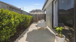 Een modern terras buiten, met een witte stoel, een gestreepte parasol en potplanten.