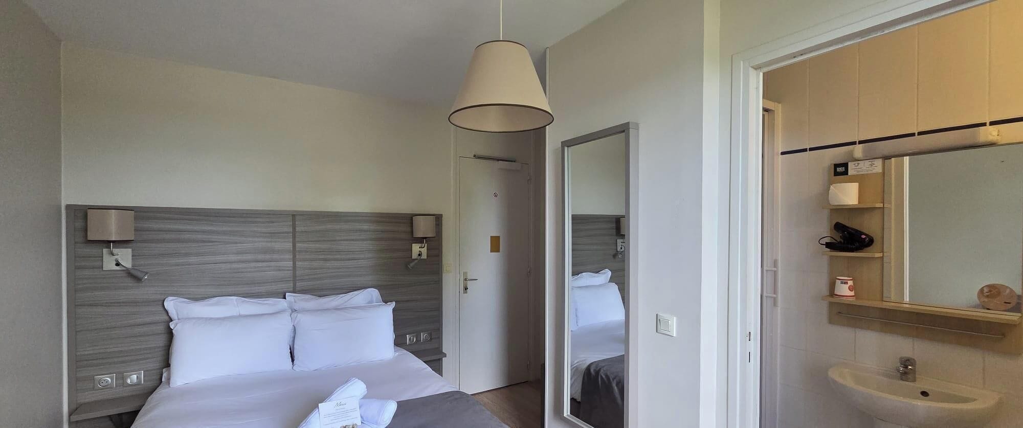 A hotel room with a bed, a mirror, a sink, and a door leading to another room.