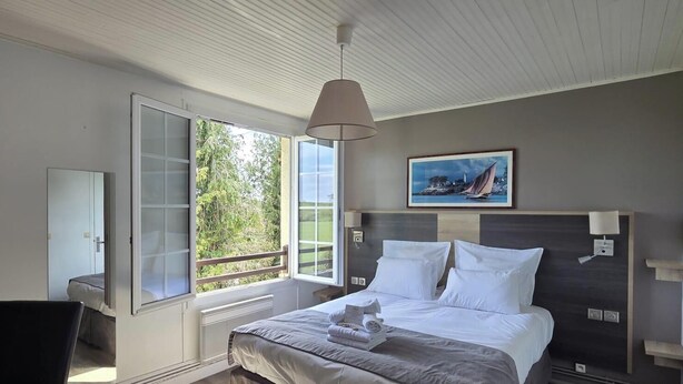 A hotel room with a bed, bedside table, lamp, and a painting on the wall. - LOGIS AUBERGE DES AULNETTES (Houlgate)