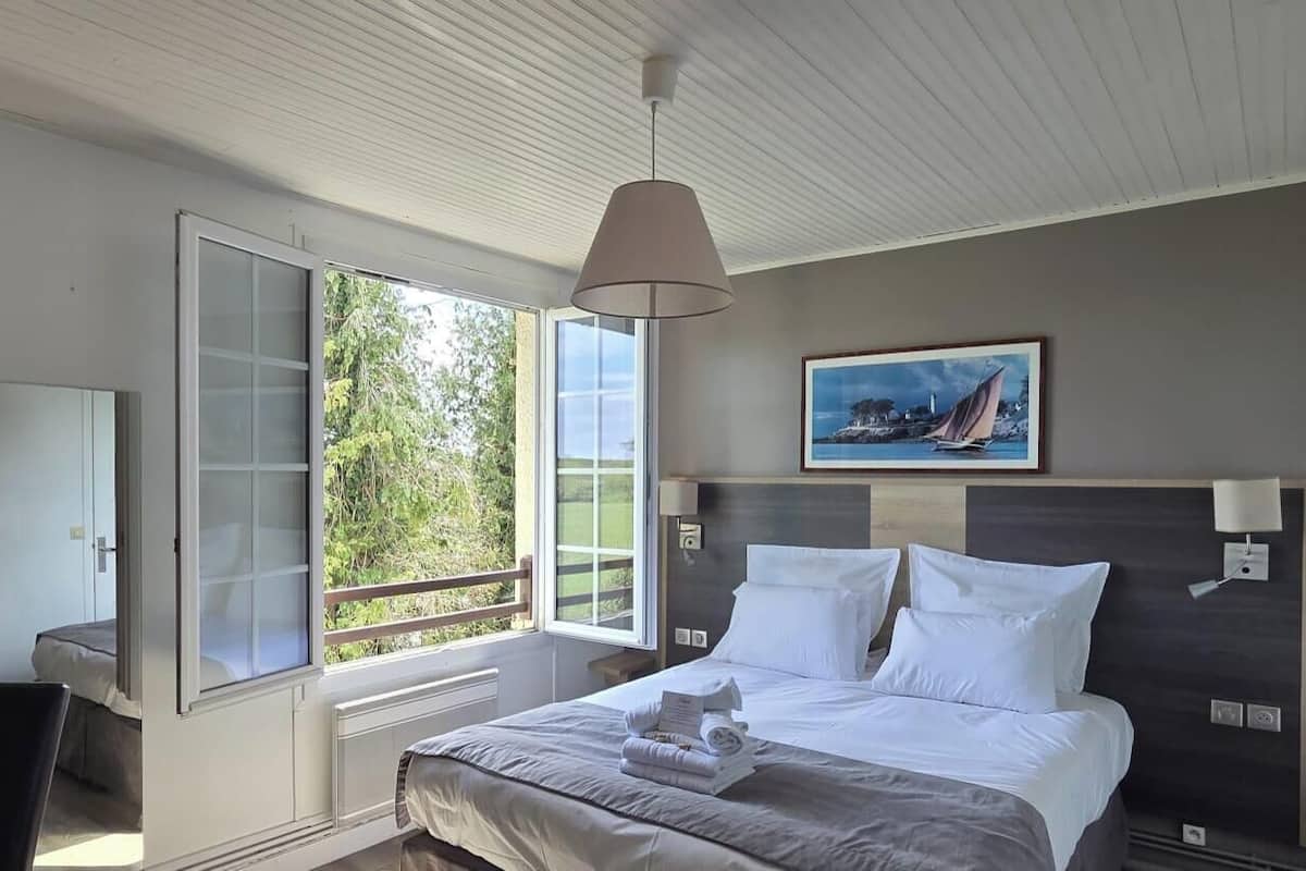 A hotel room with a bed, bedside table, lamp, and a painting on the wall.