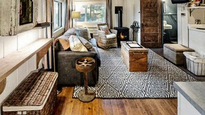 A rustic cabin interior with a wooden ceiling, a sofa, a patterned rug, and a television. - Sprucewold Beach House | Romantic Coastal Escape (Boothbay Harbor)