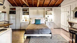 A bedroom with a bed, a dresser, a nightstand, a window, and a wooden ceiling. - Sprucewold Beach House | Romantic Coastal Escape (Boothbay Harbor)