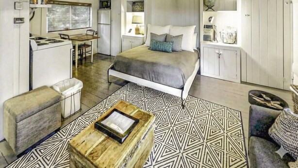 A cozy room with a bed, a desk, a kitchenette, and a ceiling fan. - Sprucewold Beach House | Romantic Coastal Escape (Boothbay Harbor)