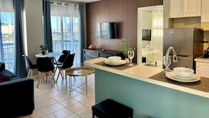 A modern hotel room with a dining area, kitchenette, and a large window offering a city view. - Ultimate Remodeled 2BR Condo at Enclave Suites (Orlando)