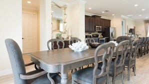 Un comedor con una mesa de madera oscura y sillas a juego, un cuenco decorativo sobre la mesa y una cocina al fondo.