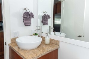 A bathroom with a white sink, granite countertop, and a large mirror. There are two towels hanging on towel rings above the sink. - Chic SD Basecamp - Walk to Downtown (San Diego)