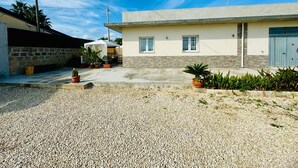 A residential area with a house featuring a concrete facade, a garage, and a gravel driveway. - GAETA HOUSE (Cicirata)