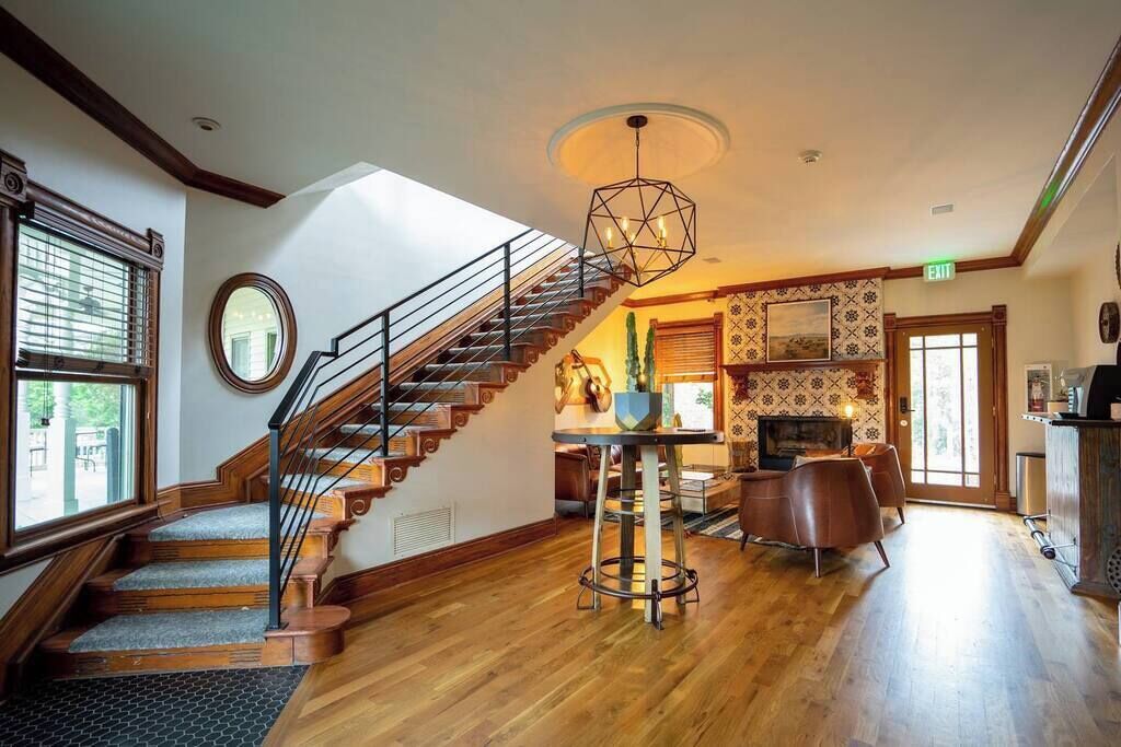 Un amplio salón con escalera de madera, un espejo redondo, una mesa de comedor con sillas y una lámpara colgante moderna.