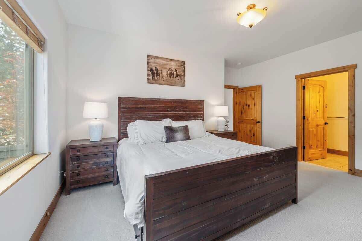 Une chambre à coucher avec un lit en bois, deux tables de chevet avec des lampes, une fenêtre et une porte donnant sur une autre pièce.