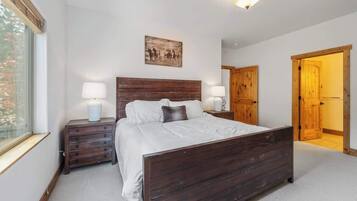 Une chambre à coucher avec un lit en bois, deux tables de chevet avec des lampes, une fenêtre et une porte donnant sur une autre pièce.