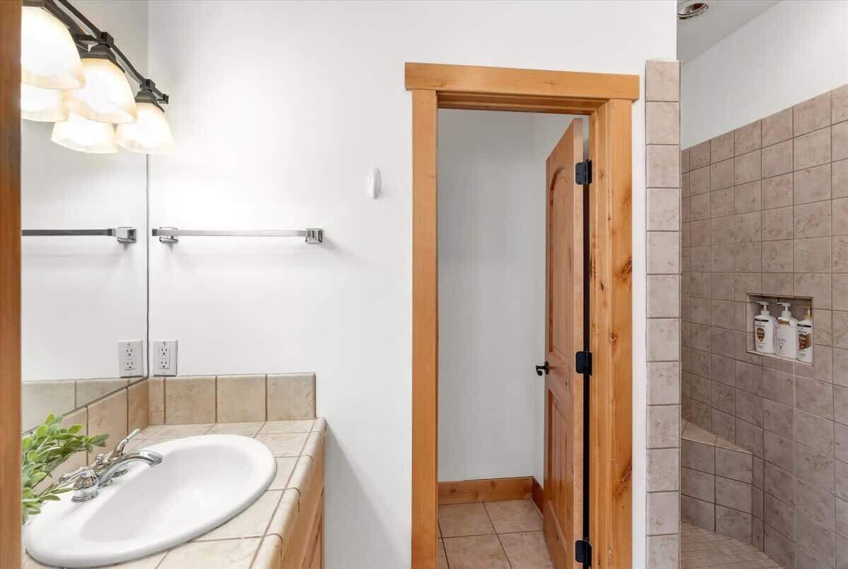 Une salle de bain avec un lavabo blanc, un miroir et un espace douche aux carreaux beiges.