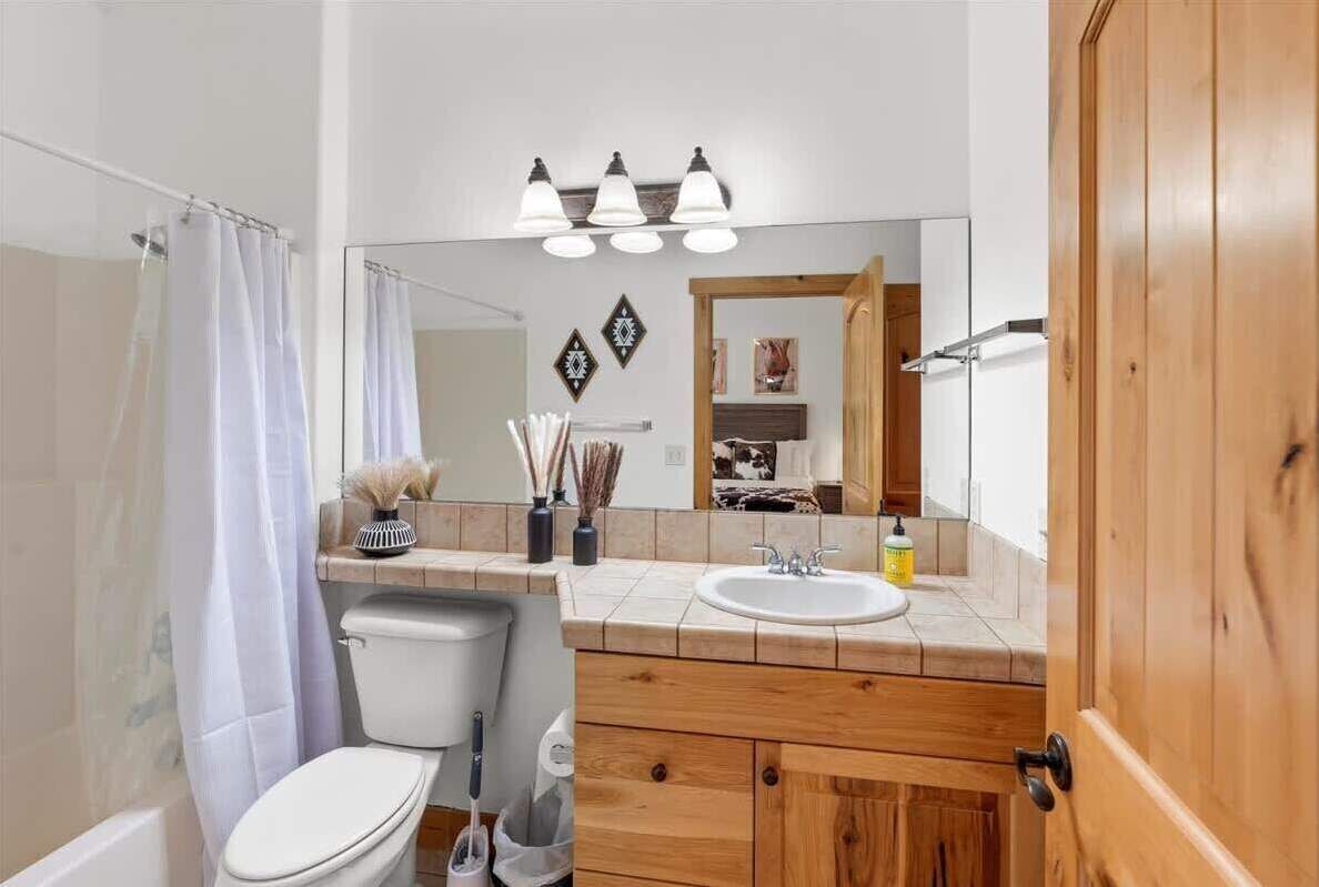 A bathroom with a toilet, sink, and mirror. There are decorative items on the counter and a shower curtain.