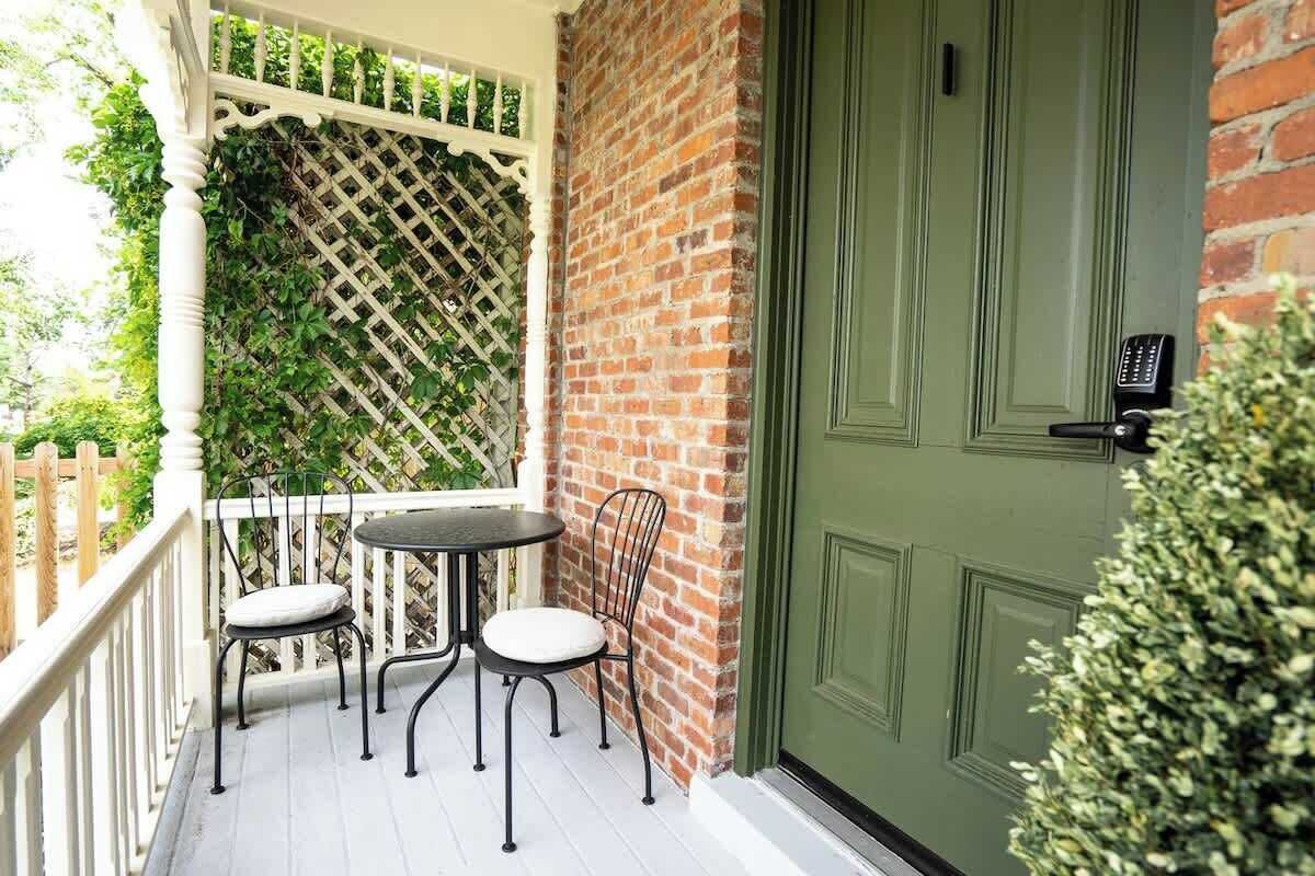 A balcony with a table and chairs, a green door, and a brick wall.