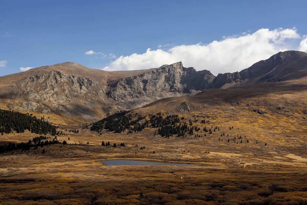 Un paisaje montañoso con cielo despejado, un lago pequeño y árboles dispersos.