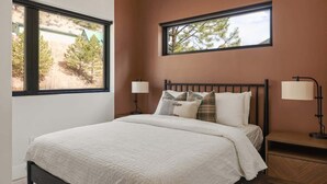 Un dormitorio con cama, dos lámparas de noche, una mesita de noche y dos ventanas.