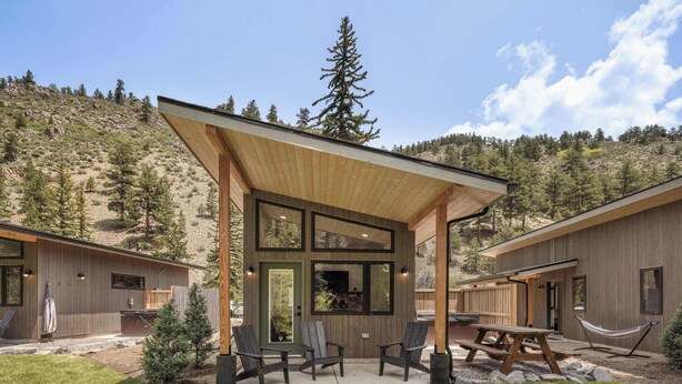A modern cabin with a covered patio, outdoor seating, and a view of a forested hillside. - Modern Mountain Studio | Hot Tub | Lostfork (Grant)