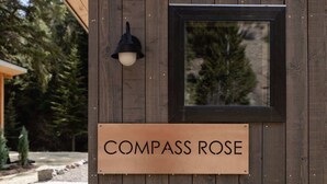 A wooden exterior wall with a sign reading "COMPASS ROSE" and a black wall-mounted light fixture. - Modern Mountain Studio | Hot Tub | Lostfork (Grant)